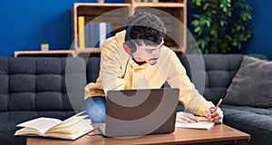 Young caucasian man using laptop and headphones studying at home