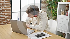 Young caucasian man using laptop and headphones writing on notebook at dinning room