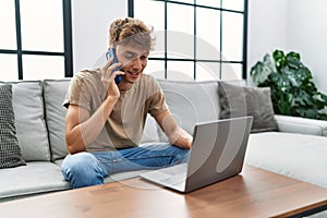 Young caucasian man using laptop talking on the smartphone at home
