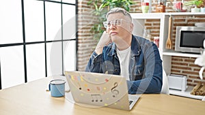 Young caucasian man using laptop thinking at dinning room