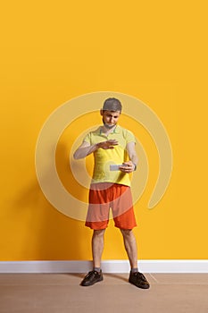 Young caucasian man using smartphone. Full body length portrait isolated over yellow background.