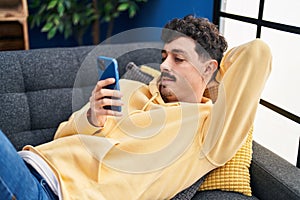 Young caucasian man using smartphone lying on sofa at home