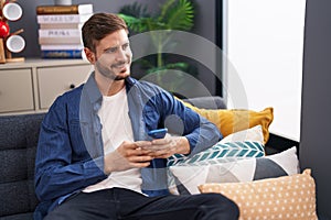 Young caucasian man using smartphone sitting on sofa at home