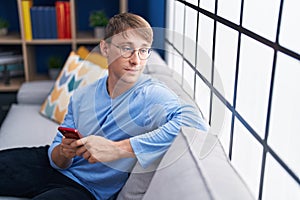 Young caucasian man using smartphone sitting on sofa at home