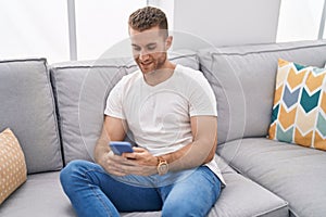 Young caucasian man using smartphone sitting on sofa at home