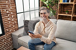 Young caucasian man using smartphone sitting on sofa at home