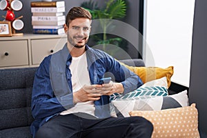 Young caucasian man using smartphone sitting on sofa at home