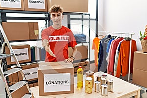 Young caucasian man volunteer holding donations box smiling friendly offering handshake as greeting and welcoming