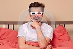 Young caucasian man watching TV at home in the bed in 3d glasses being excited and amuzed
