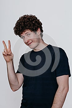 Young Caucasian man wearing a black t-shirt on a white background making a peace gesture, pursing his lips and showing a