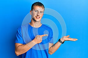 Young caucasian man wearing casual blue t shirt amazed and smiling to the camera while presenting with hand and pointing with