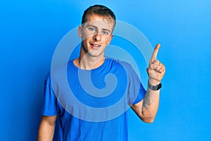 Young caucasian man wearing casual blue t shirt with a big smile on face, pointing with hand finger to the side looking at the