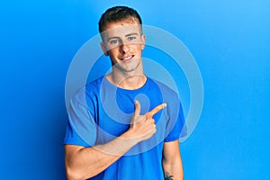 Young caucasian man wearing casual blue t shirt cheerful with a smile on face pointing with hand and finger up to the side with