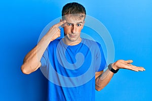 Young caucasian man wearing casual blue t shirt confused and annoyed with open palm showing copy space and pointing finger to