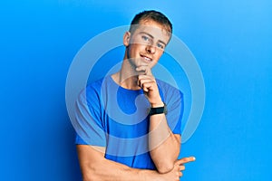 Young caucasian man wearing casual blue t shirt looking confident at the camera smiling with crossed arms and hand raised on chin