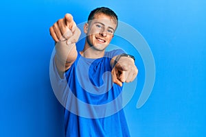 Young caucasian man wearing casual blue t shirt pointing to you and the camera with fingers, smiling positive and cheerful