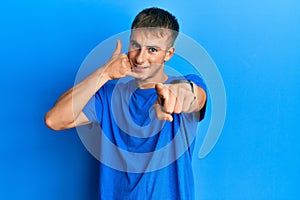 Young caucasian man wearing casual blue t shirt smiling doing talking on the telephone gesture and pointing to you
