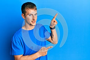 Young caucasian man wearing casual blue t shirt smiling and looking at the camera pointing with two hands and fingers to the side