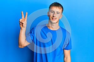 Young caucasian man wearing casual blue t shirt smiling looking to the camera showing fingers doing victory sign