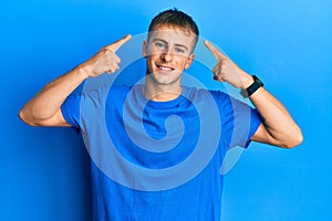 Young caucasian man wearing casual blue t shirt smiling pointing to head with both hands finger, great idea or thought, good