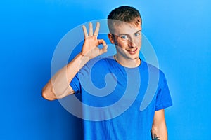 Young caucasian man wearing casual blue t shirt smiling positive doing ok sign with hand and fingers