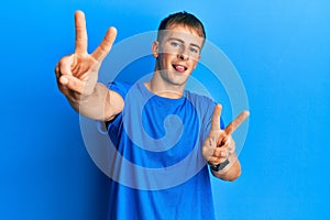 Young caucasian man wearing casual blue t shirt smiling with tongue out showing fingers of both hands doing victory sign