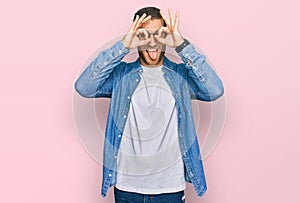 Young caucasian man wearing casual clothes doing ok gesture like binoculars sticking tongue out, eyes looking through fingers