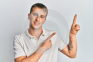 Young caucasian man wearing casual white polo smiling and looking at the camera pointing with two hands and fingers to the side