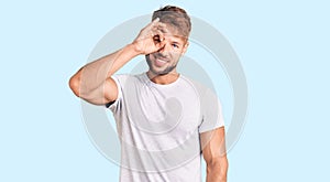 Young caucasian man wearing casual white tshirt doing ok gesture with hand smiling, eye looking through fingers with happy face
