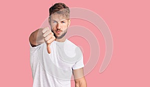 Young caucasian man wearing casual white tshirt looking unhappy and angry showing rejection and negative with thumbs down gesture