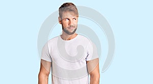 Young caucasian man wearing casual white tshirt smiling looking to the side and staring away thinking
