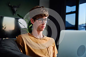 Young caucasian man wearing eyeglasses using laptop in living room on sofa at home