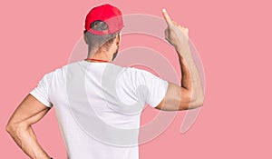 Young caucasian man wearing lifeguard t shirt holding whistle posing backwards pointing ahead with finger hand