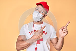 Young caucasian man wearing lifeguard t shirt using medical mask smiling and looking at the camera pointing with two hands and