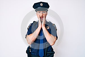 Young caucasian man wearing police uniform afraid and shocked, surprise and amazed expression with hands on face