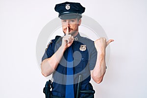 Young caucasian man wearing police uniform asking to be quiet with finger on lips pointing with hand to the side