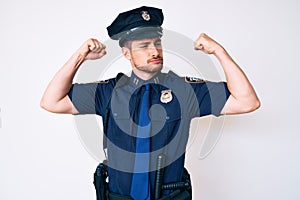 Young caucasian man wearing police uniform showing arms muscles smiling proud