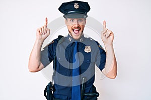 Young caucasian man wearing police uniform smiling amazed and surprised and pointing up with fingers and raised arms