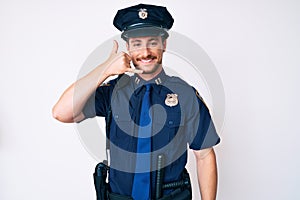 Young caucasian man wearing police uniform smiling doing phone gesture with hand and fingers like talking on the telephone