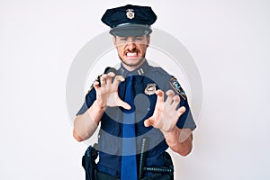 Young caucasian man wearing police uniform smiling funny doing claw gesture as cat, aggressive and sexy expression