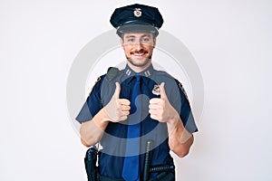 Young caucasian man wearing police uniform success sign doing positive gesture with hand, thumbs up smiling and happy