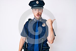Young caucasian man wearing police uniform surprised pointing with hand finger to the side, open mouth amazed expression
