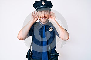 Young caucasian man wearing police uniform trying to hear both hands on ear gesture, curious for gossip