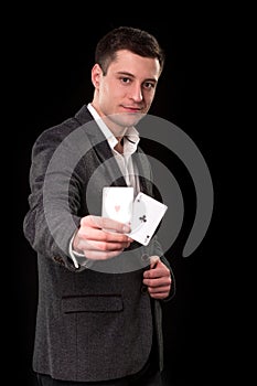 Young caucasian man wearing suit holding two aces in his hand on black background. Gambling concept. Casino