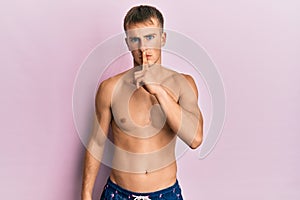 Young caucasian man wearing swimwear asking to be quiet with finger on lips