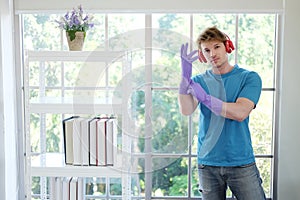 Young Caucasian man Wearing violet rubber gloves for clean of housework and relaxing for listening to music with red headphone.