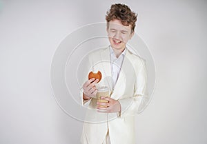 Young caucasian man in a white business suit stands with a paper Cup of coffee and a bun in his hand and suffers from severe abdom