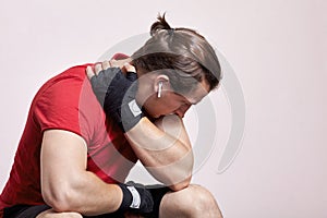 Young caucasian man with white earphones and little pony tail, in sportswear and boxing bandages sits in depressed pose. Despair m