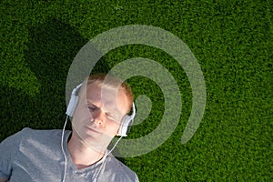 A young Caucasian man in a white T-shirt and headphones lies on an artificial lawn