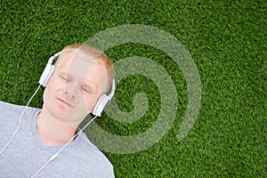 A young Caucasian man in a white T-shirt and headphones lies on an artificial lawn